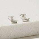 Pair of silver ripple stud earrings on a textured white surface