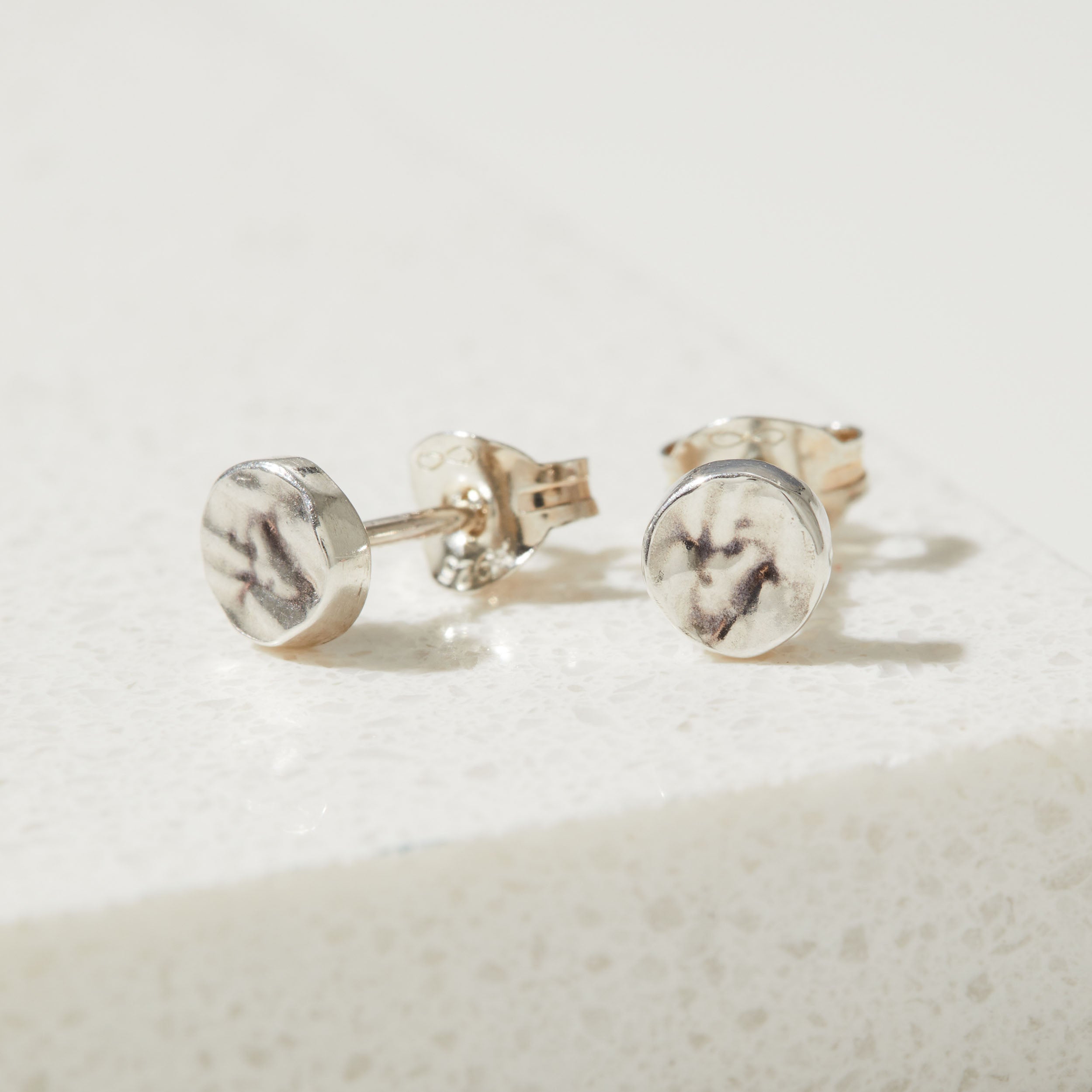 Silver bark textured stud earrings on a light beige background