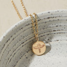 Gold necklace with a phoenix pendant on a speckled ceramic dish