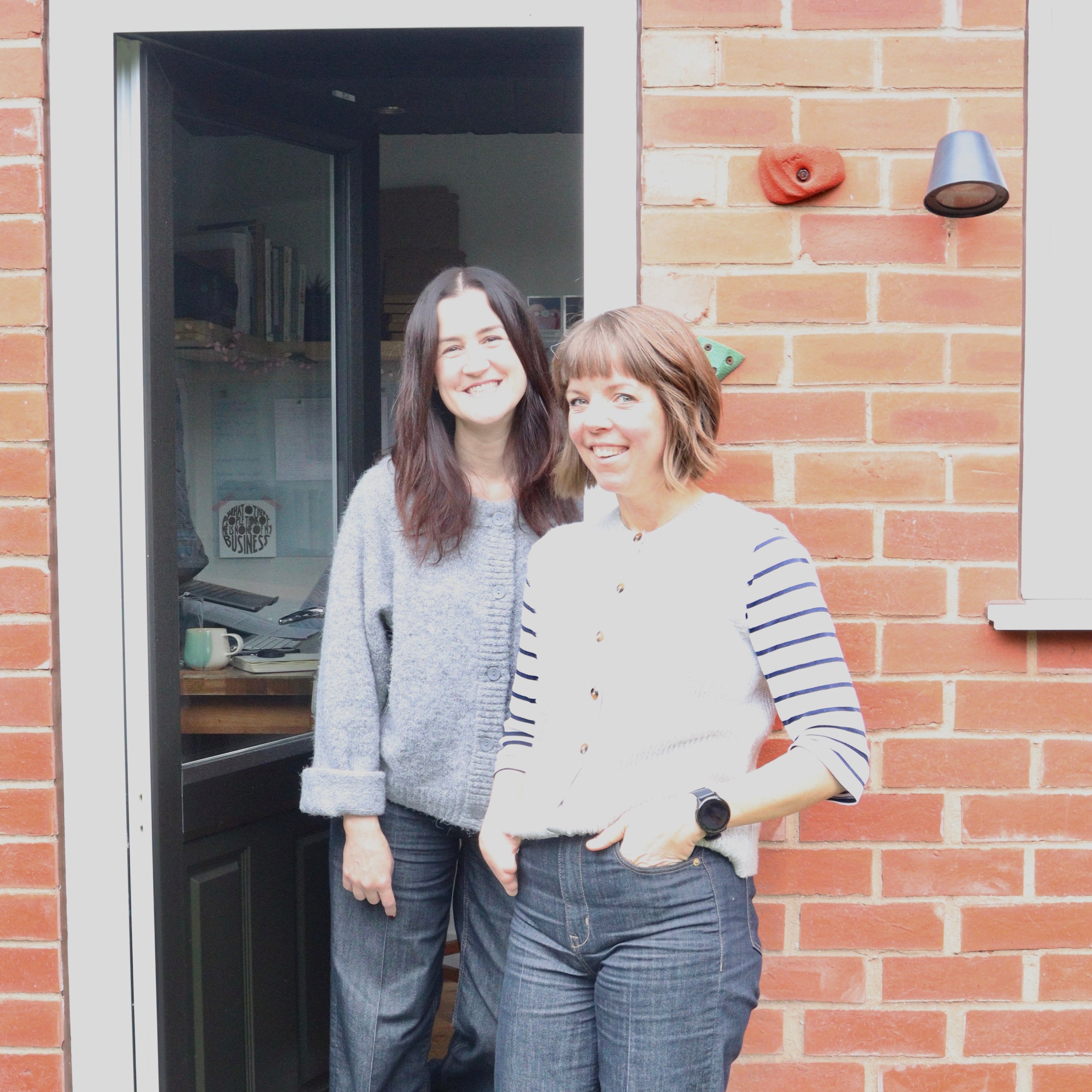 Two women standing outside a brick building with a door open.