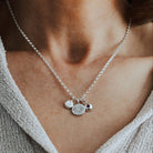 Silver necklace with heart, initial and birthstone pendants on a person wearing a light gray sweater.