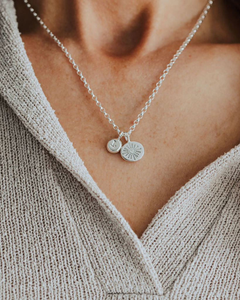 Necklace with heart and initial pendants worn by a person in a beige sweater.
