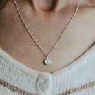 Necklace with a small initial pebble pendant on a pebble chain worn by a person in a white and brown striped sweater.
