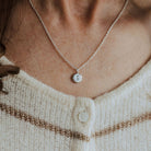 Close-up of a person wearing an initial pebble necklace on a blurred background