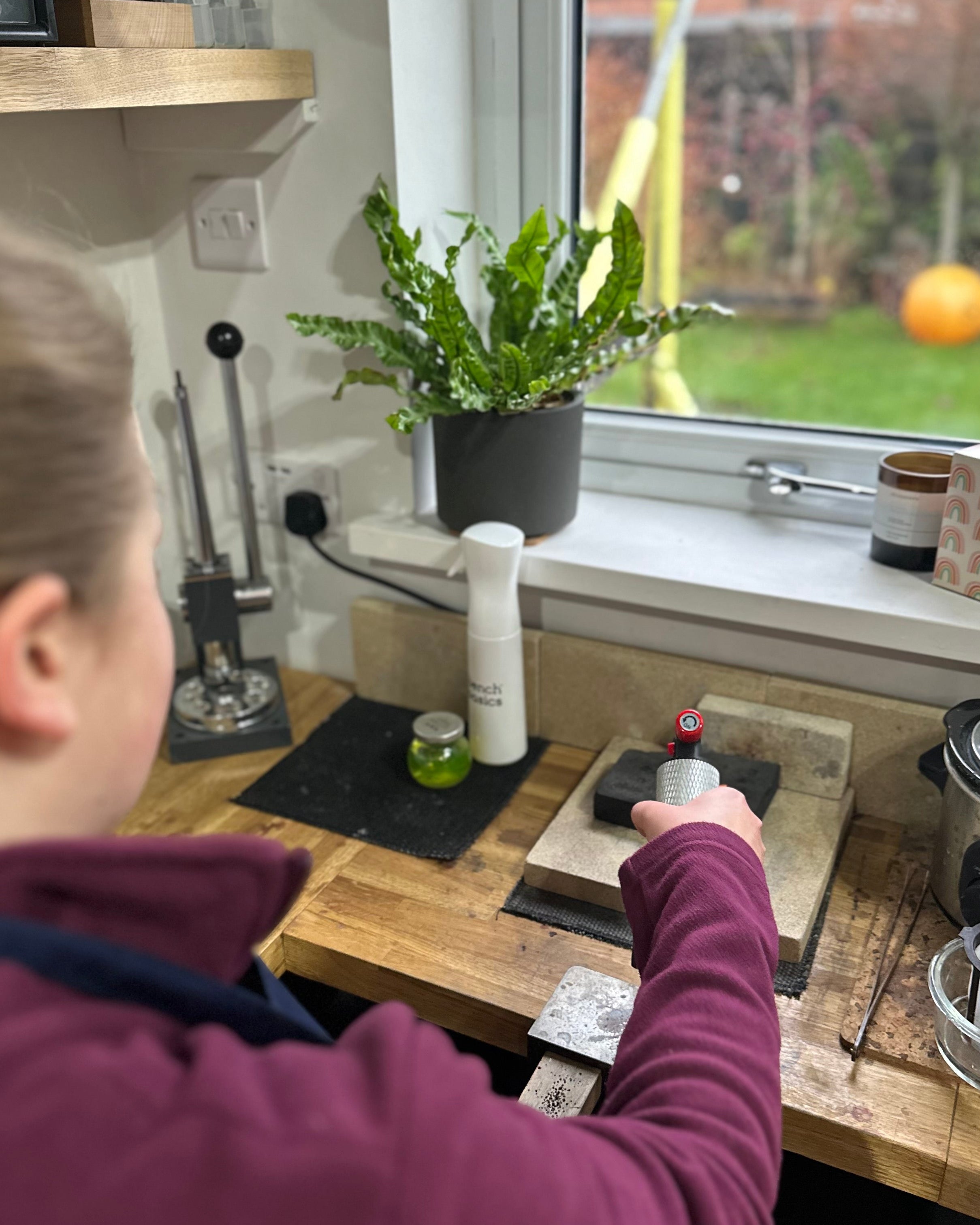 Person making jewellery with a window view of a garden.