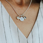 Silver necklace with pheonix, initial and birthstone charms on a person wearing a white pinstripe shirt
