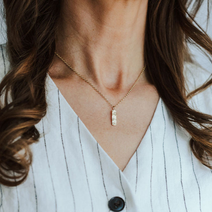 Woman wearing a tree textured gold necklace with a white top against a neutral background