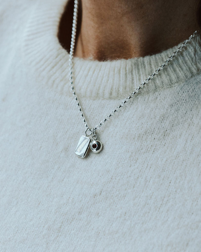Woman in a white knitted t-shirt wearing a silver feather necklace with a birthstone charm.