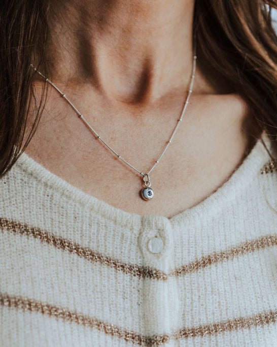Necklace with a birthstone pendant worn by a person with long hair, against a neutral background.
