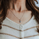 Necklace with a birthstone pendant worn by a person with long hair, against a neutral background.