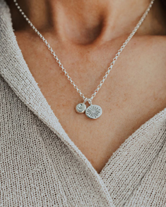 Silver necklace with two charms worn by a person in a beige sweater.