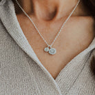 Silver necklace with two charms worn by a person in a beige sweater.