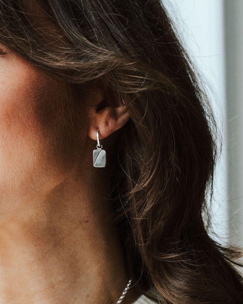 Woman with dark hair wearing a pair of hoop earrings with feather charms.