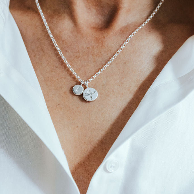 Silver necklace with round phoenix and initial pendants on a white shirt background