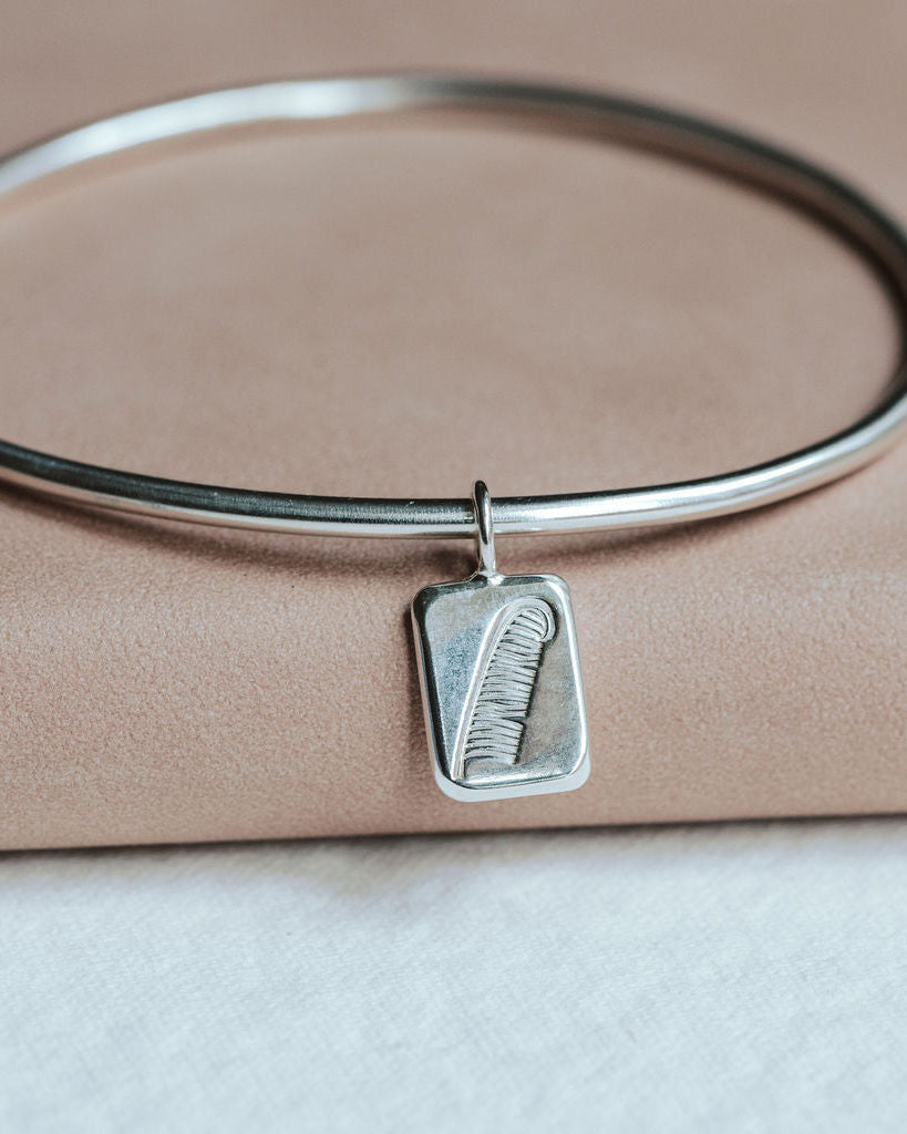 Silver bangle with a feather charm on a pink book.