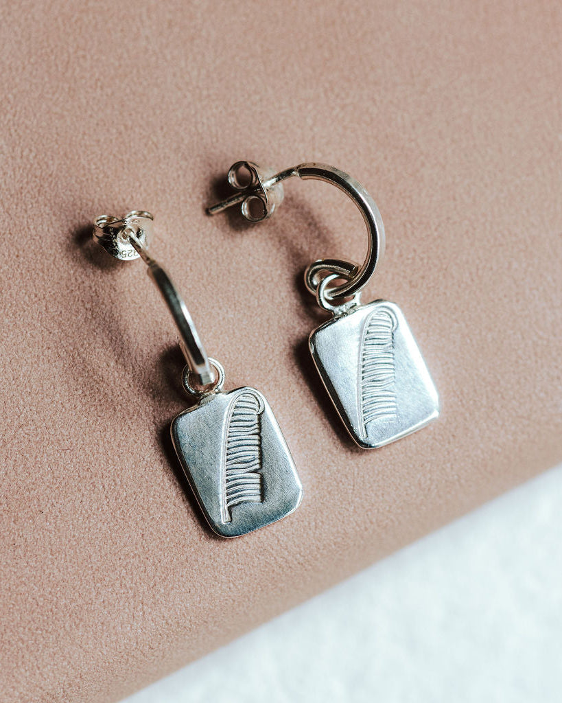 Sterling silver hoop earrings with feather charms resting on a pink book.