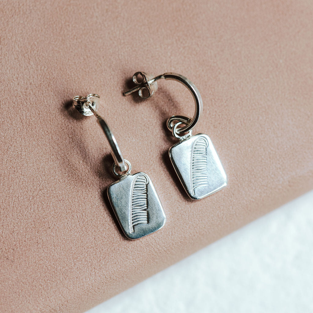 Sterling silver hoop earrings with feather charms resting on a pink book.