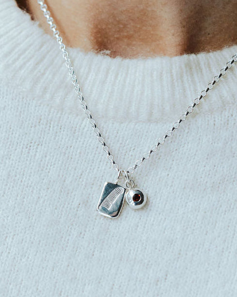 Woman in a white knitted t-shirt wearing a charm necklace with a feather design on it and a birthstone.