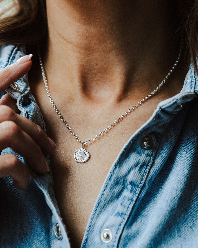 Woman in a denim shirt wearing a necklace with a sunrise design on it.