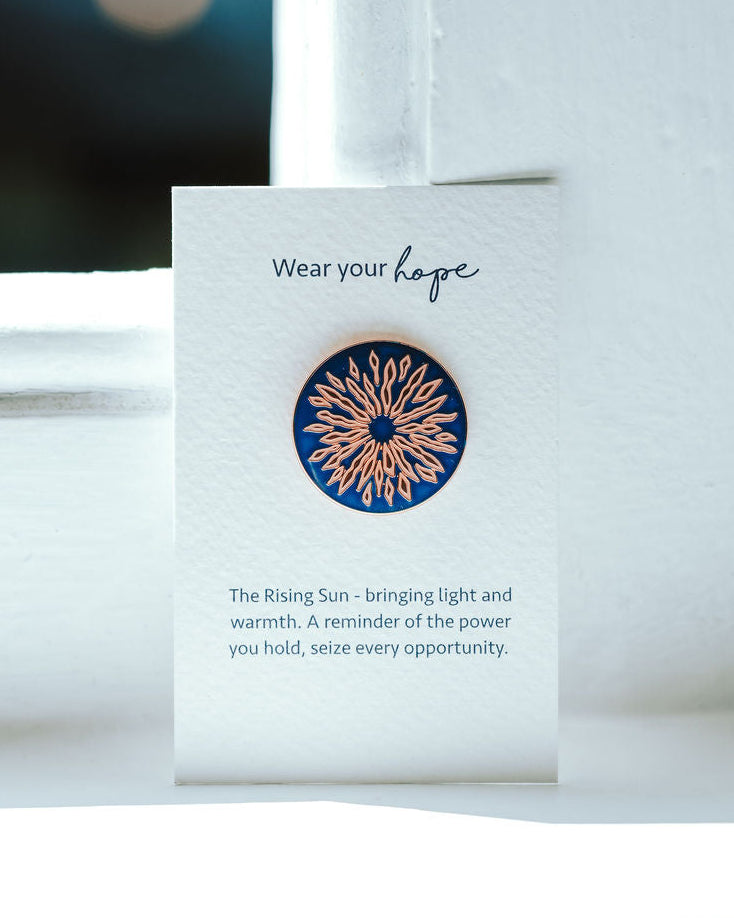 Sunrise design on a blue pin badge on a white card.