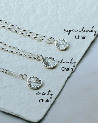 Three silver necklaces with different chain styles on a textured surface.