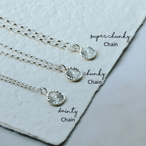 Three silver necklaces with different chain styles on a textured surface.