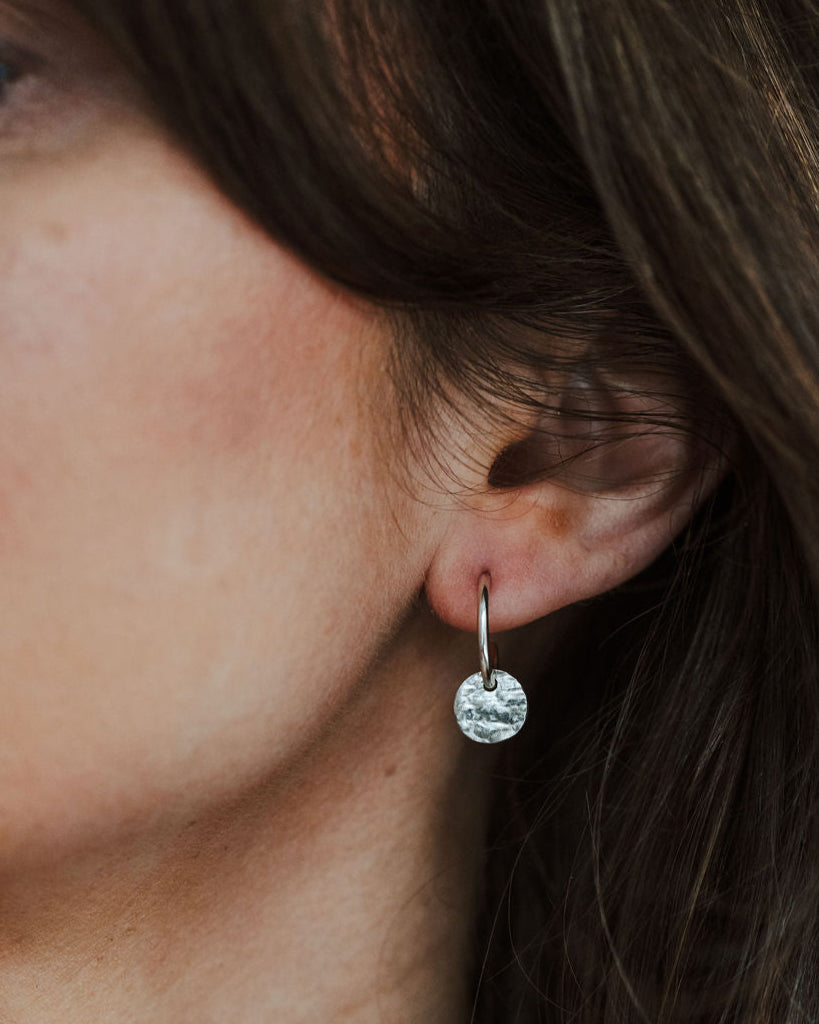 Close-up of a person wearing a silver earring with a tree bark textured charm.