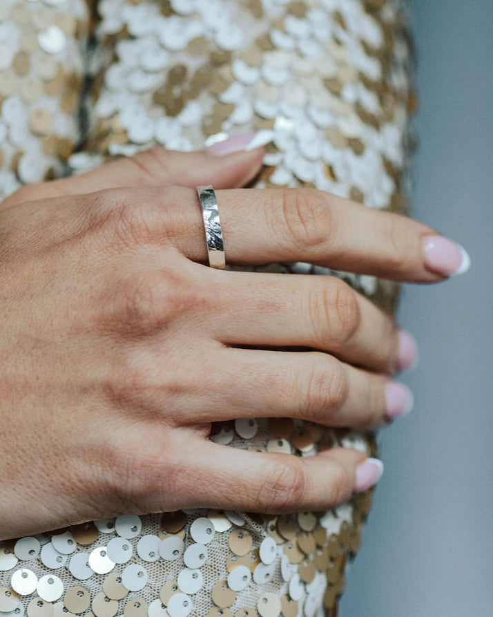 Close-up of a hand wearing a tree bark textured stacking ring on a sequinned fabric background