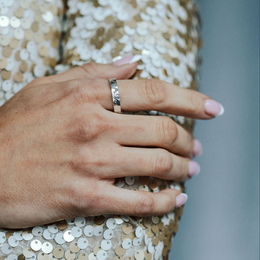 Close-up of a hand wearing a tree bark textured stacking ring on a sequinned fabric background