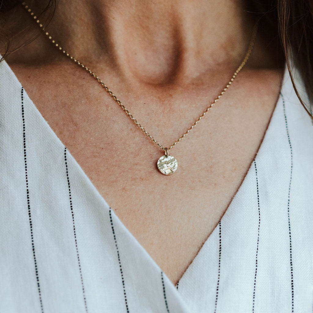 Necklace with a bark textured pendant worn by a person in a white shirt with black stripes.