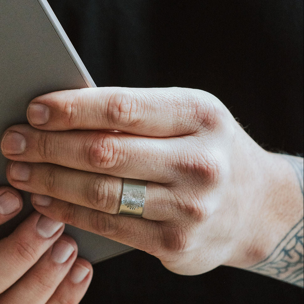 Man wearing a ring with sunrise design holding a grey notebook.