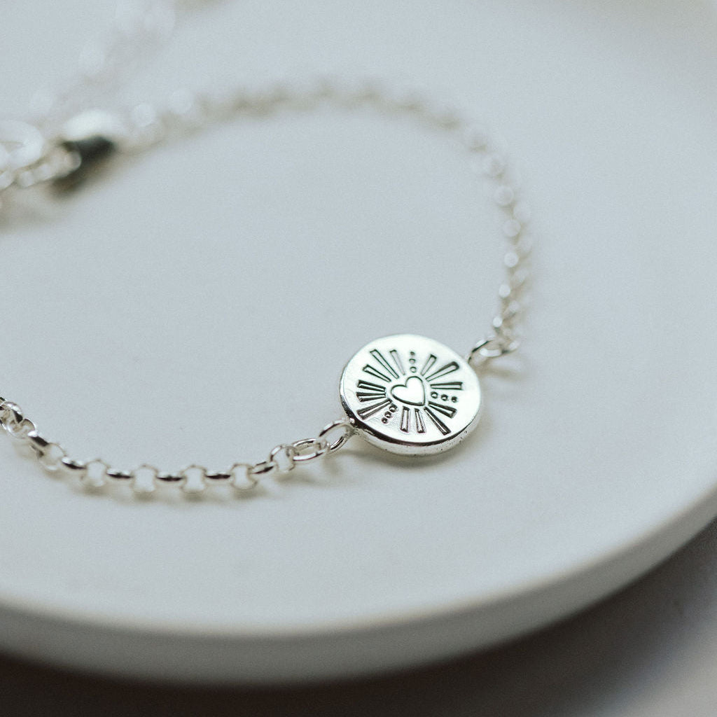 Silver bracelet with a circular heart pendant on a white plate
