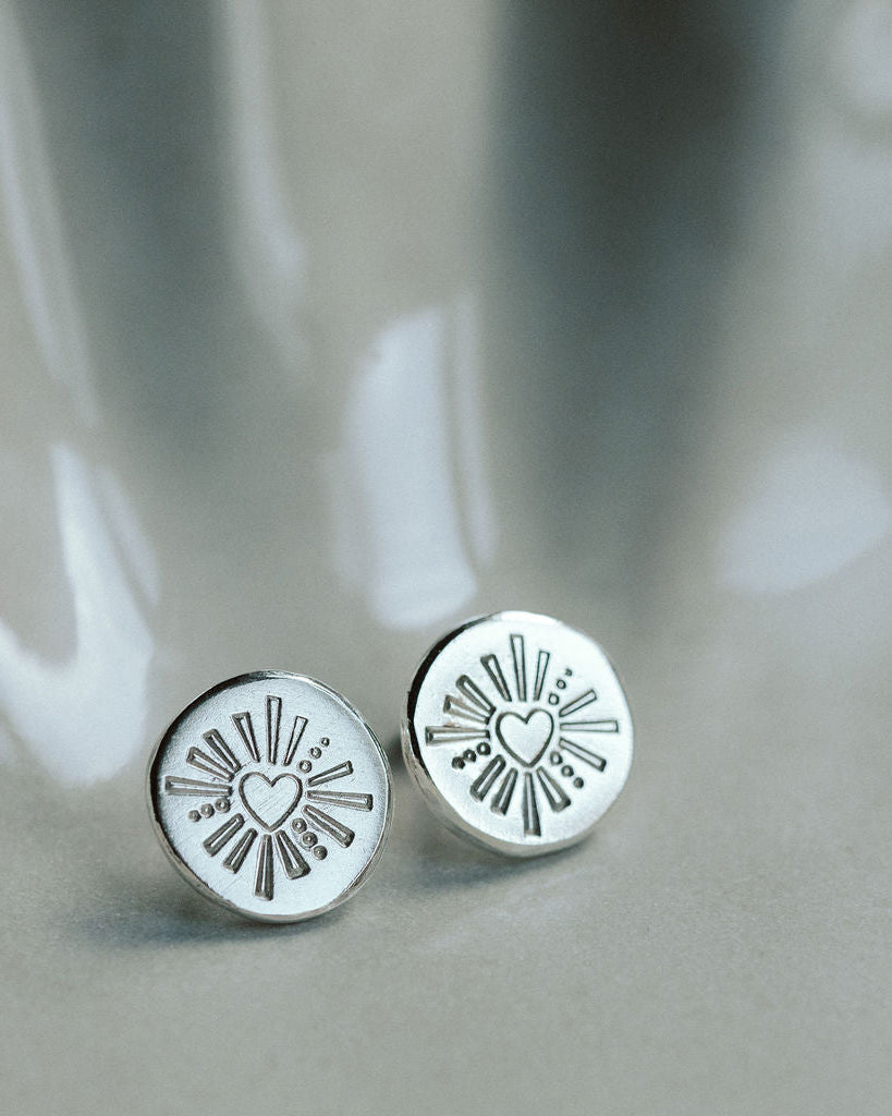 Silver round earrings with heart designs on a gray surface