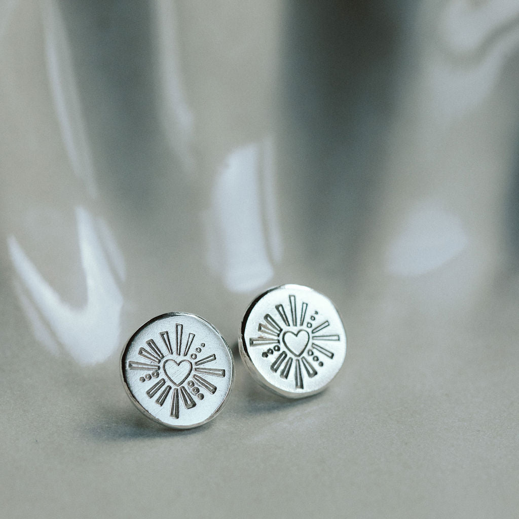 Silver round earrings with heart designs on a gray surface