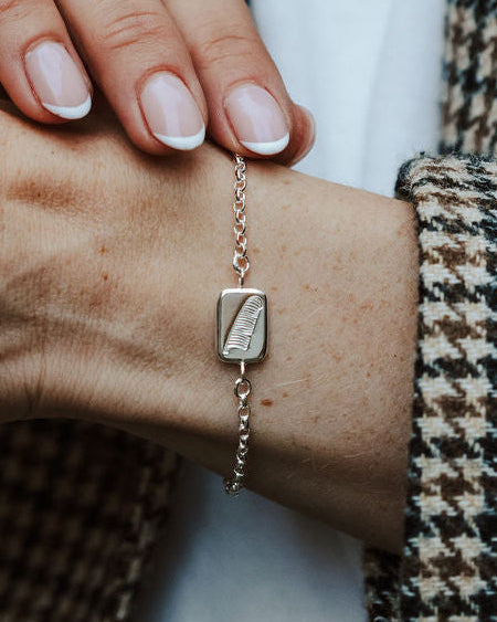 lady wearing a silver bracelet with a square charm and a feather motif