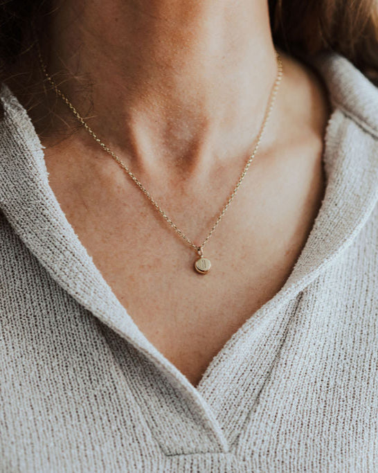 Close-up of a person wearing a gold necklace with initial pendant.