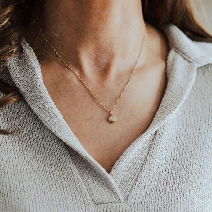 Close-up of a person wearing a gold necklace with initial pendant.