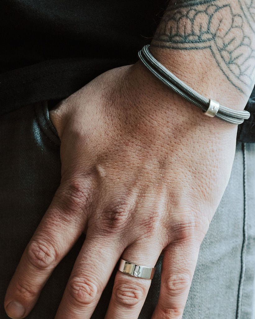 Hand with a ring and bracelet, wearing a black leather jacket and gray pants.