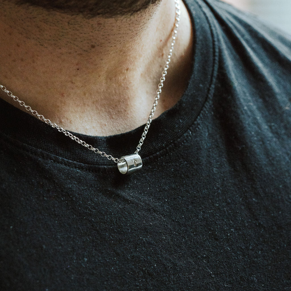 Person wearing a black shirt with a necklace featuring a small pendant.