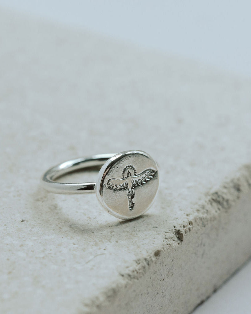Silver ring with a phoenix design on a textured stone surface