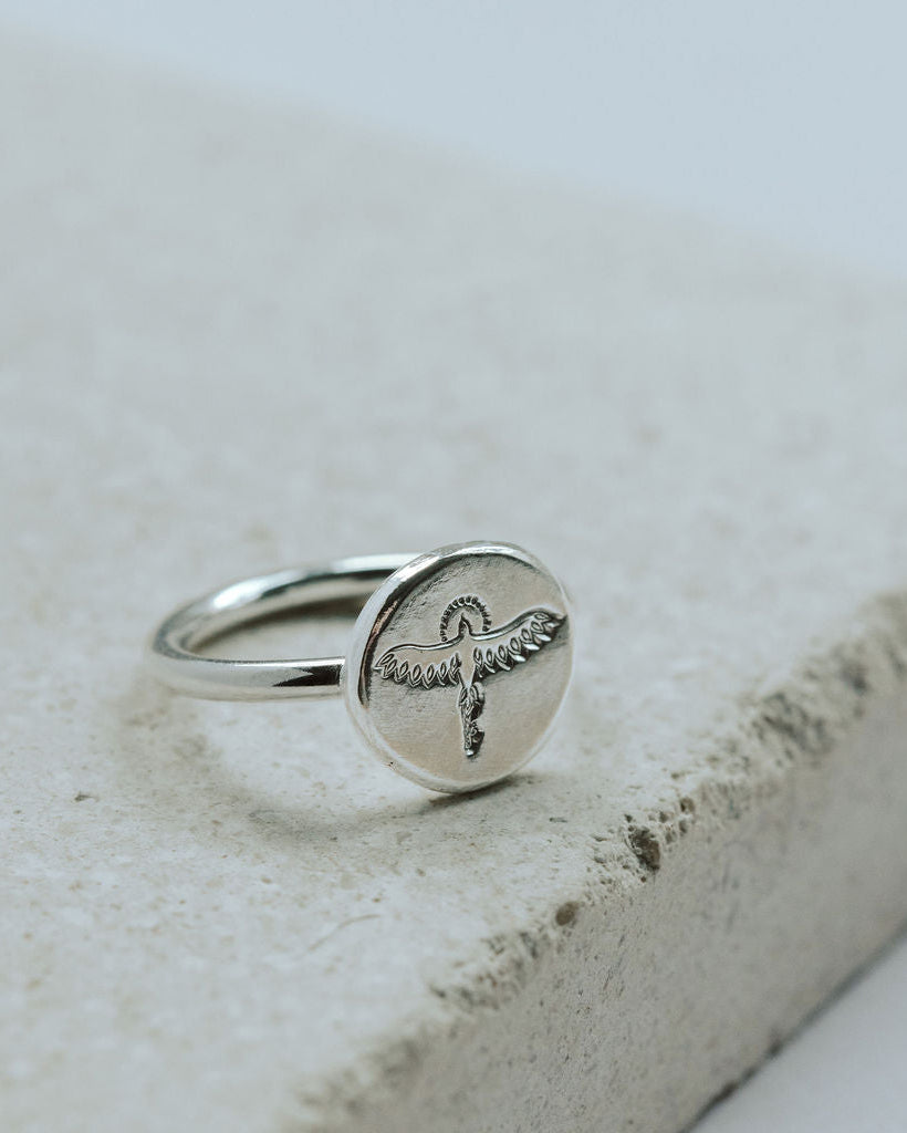 Silver ring with a phoenix design on a textured stone surface