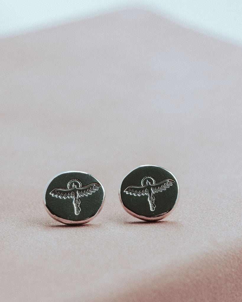 Silver round earrings with silver designs on a pink surface