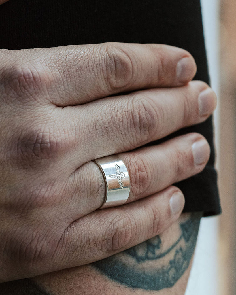 Hand wearing a silver ring with tattoos on the arm, blurred background