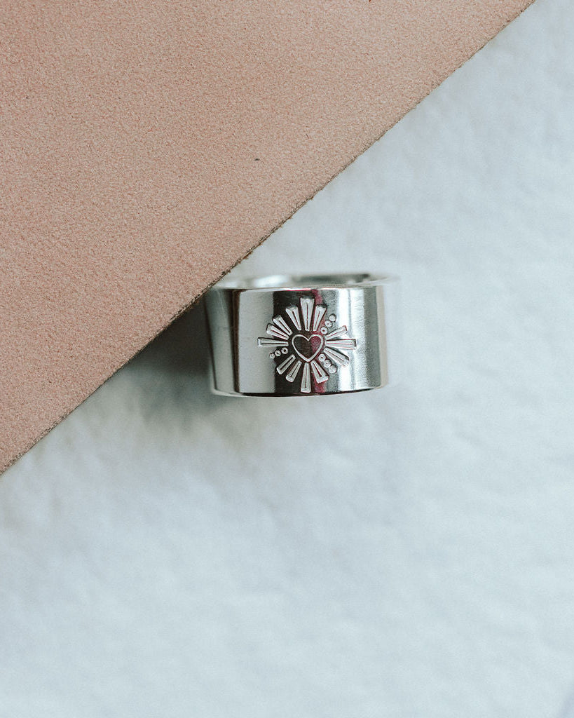 Silver ring with a heart design on a light pink and white background