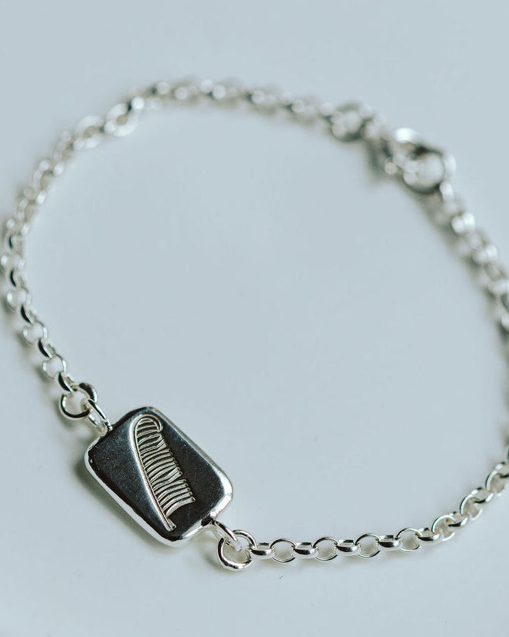 silver bracelet with a charm with a feather motif on a white dish