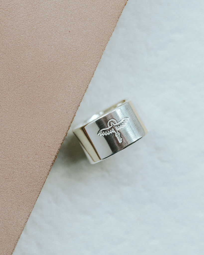 Silver ring with phoenix design on a beige and white background