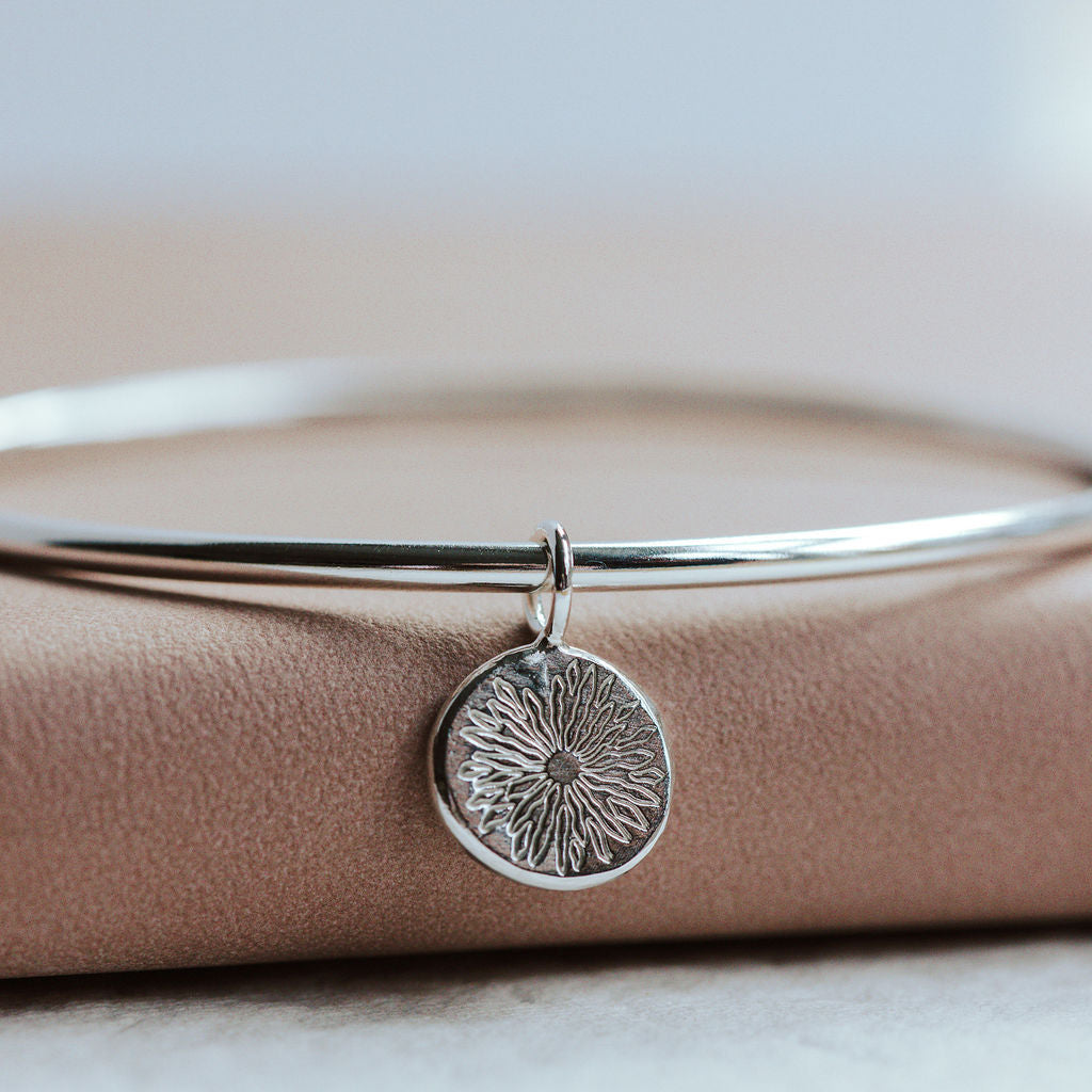 Silver bangle with a circular sunrise pendant on a beige surface