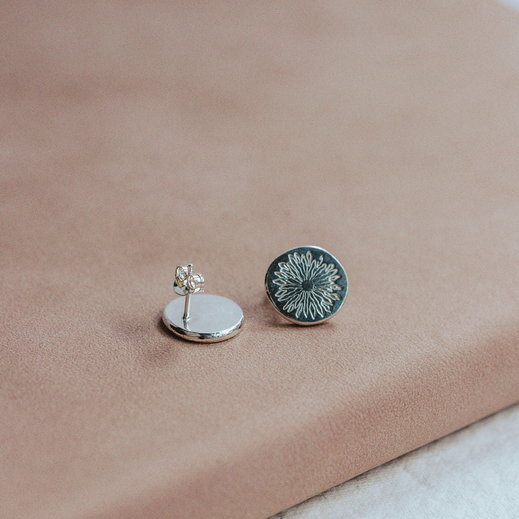 Pair of silver earrings with sunrise design on a beige surface