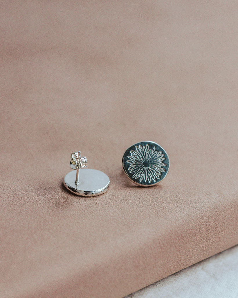 Pair of silver earrings with sunrise design on a beige surface