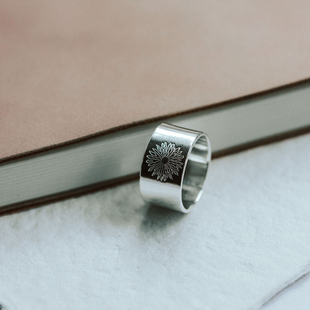 Silver ring with sunrise design on a marble surface